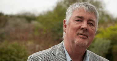 A man in a garden in a suit looking at the camera