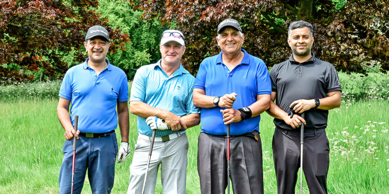 St Clare Hospice Golf Day attendees are pictured standing in a line with their golf clubs. They smile directly at the camera.