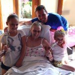 Father and daughters sitting on mother's hospital bed