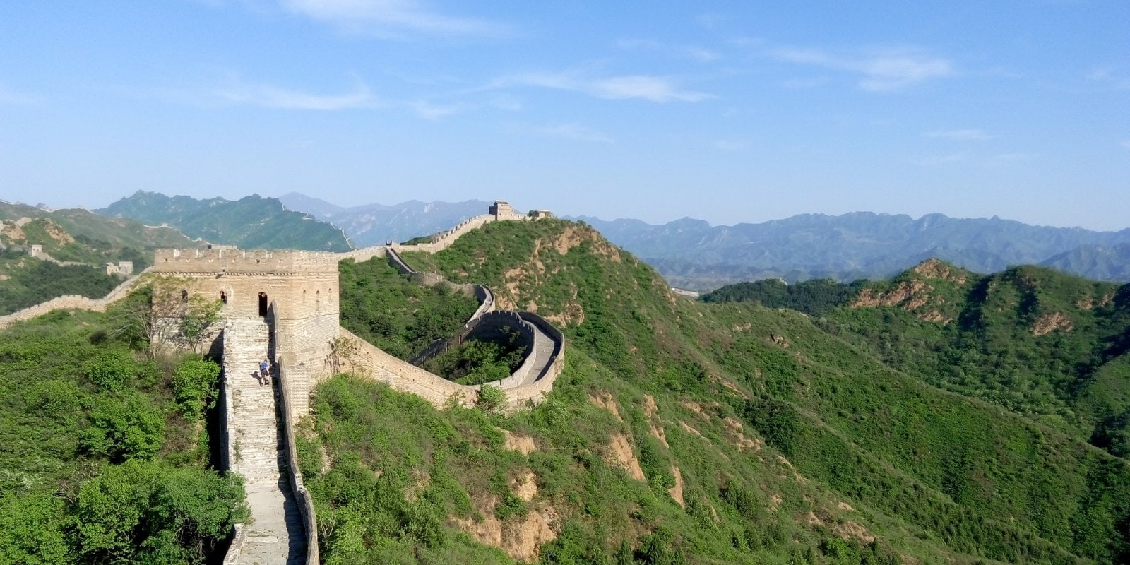 A shot of the Great Wall of China can be seen as it stretches across the photo. The sky is blue as the sunshine reflects off the historic wal.