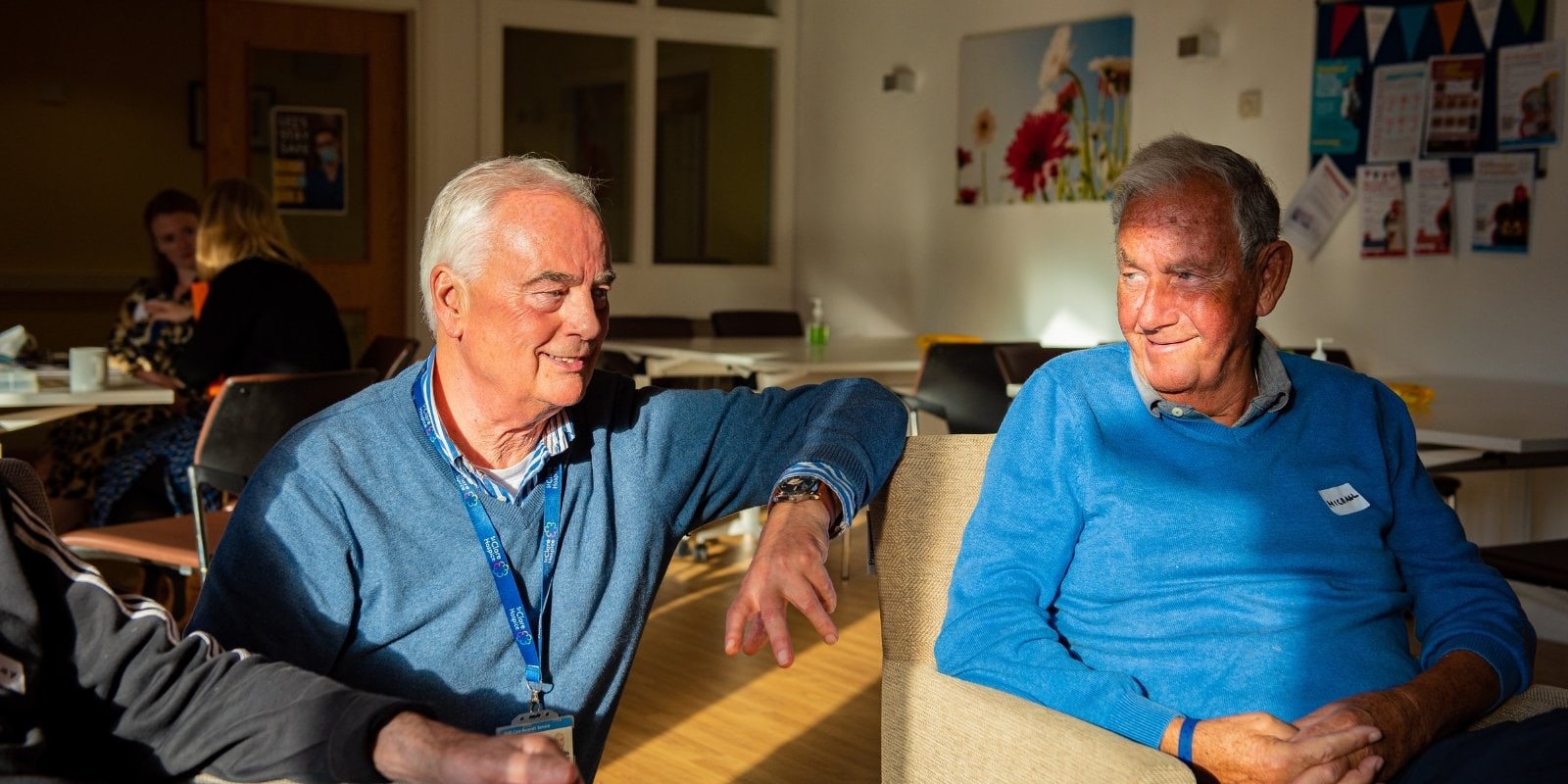 A St Clare Bereavement Café Facilitator can be seen sat with an attendee. They smile in conversation together.