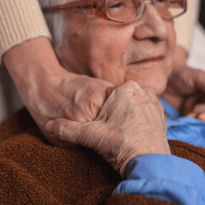 An elderly person holds a carer's hands