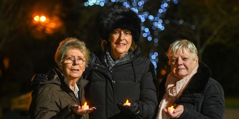 A group of three ladies standing in front of the Light up a Life tree with their candles celebrating someone special to them at St Clare Hospice.