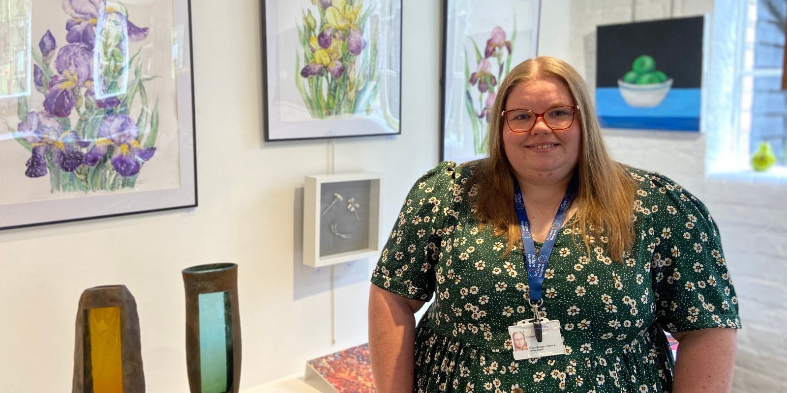 Photo of Chloe Rich, St Clare Hospice Project Manager for Patient and Family Support Services is pictured at Parndon Mill in front of some of the artwork made by The Unspoken Conversation artists. She smiles to camera.