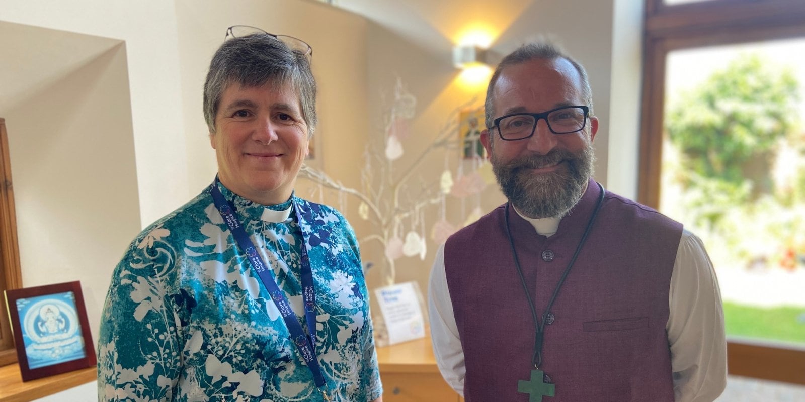 Photo of Becky Leach, St Clare Hospice Chaplain, at her licensing ceremony with Bishop of Bradwell, the Right Reverend Adam Atkinson. Both smile at the camera as they stand next to one another.