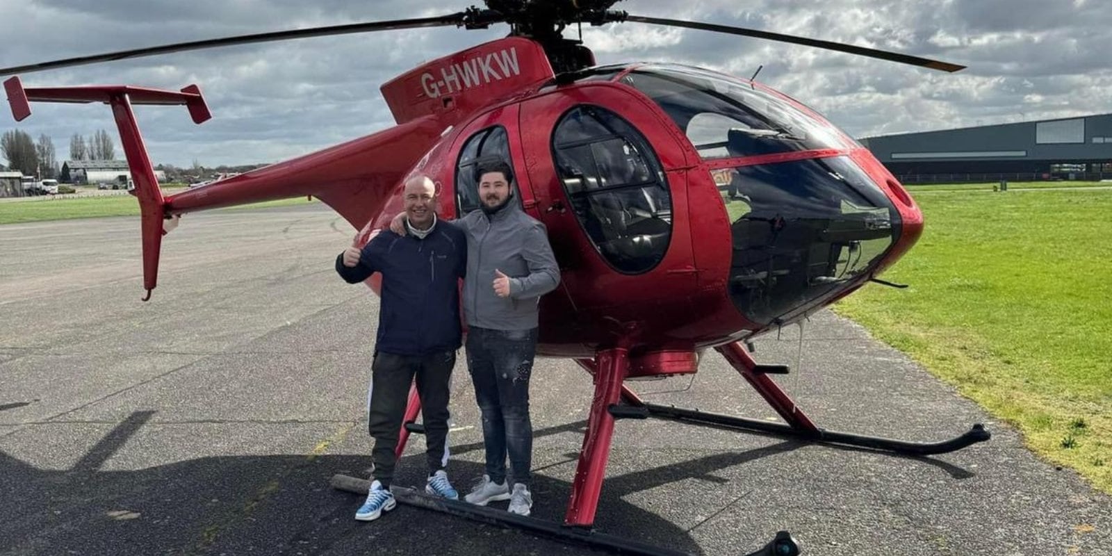 Photo of Bradley with his dad Bob in front of a helicopter. They both smile and hold their thumbs up to the camera.