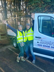 Two Christmas tree collection volunteers - lady is pictured left, gentleman on the right - excitedly raising their arms above their head while collecting Christmas trees for St Clare.