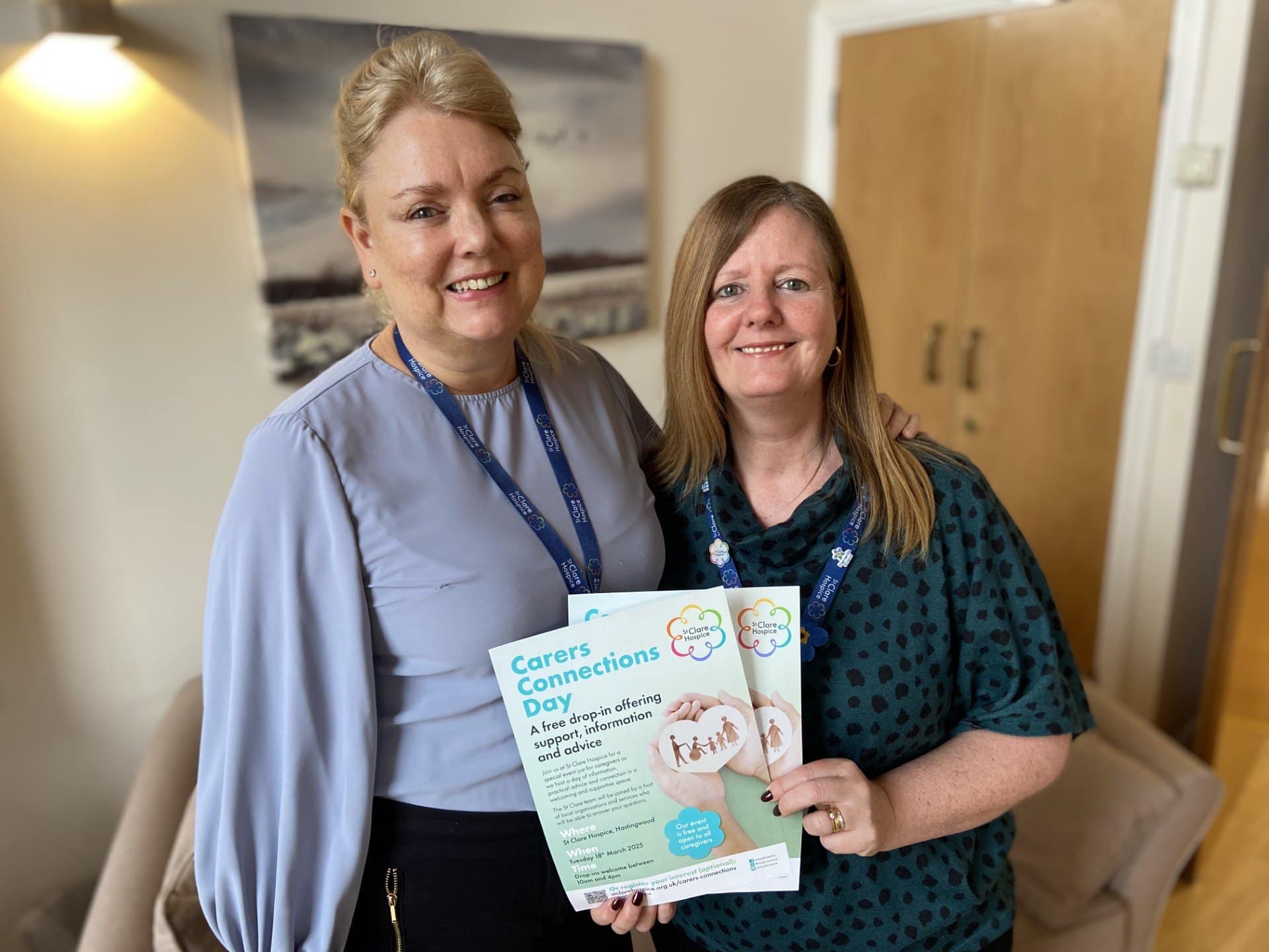 Two women stand together holding a poster advertising an event for carers