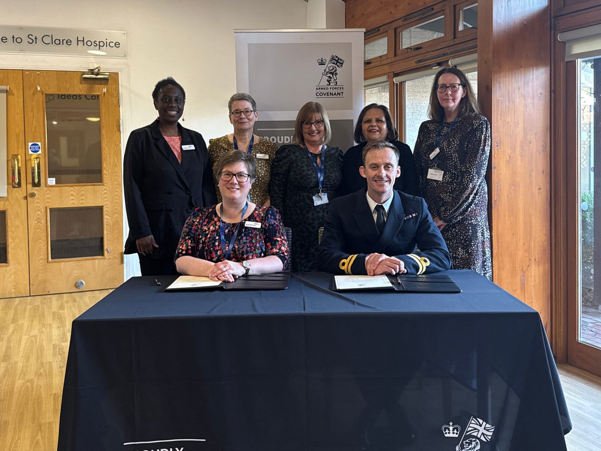 A group of people gather round a table to sign a document set out in front of them in a black leather folder