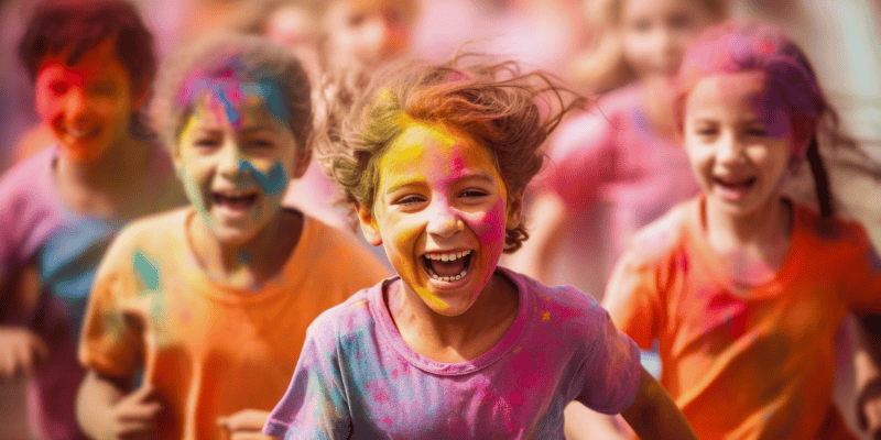 Photo of young children running towards a camera while they are covered in paint. They smile as they run.