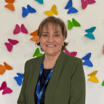 Photo of Director of People & Communities Helen Grubb. She is pictured smiling at the camera while wearing a khaki blazer and black top. She has short brunette hair.