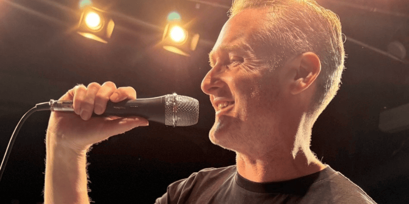 Photo of Jim singing into a microphone while smiling.