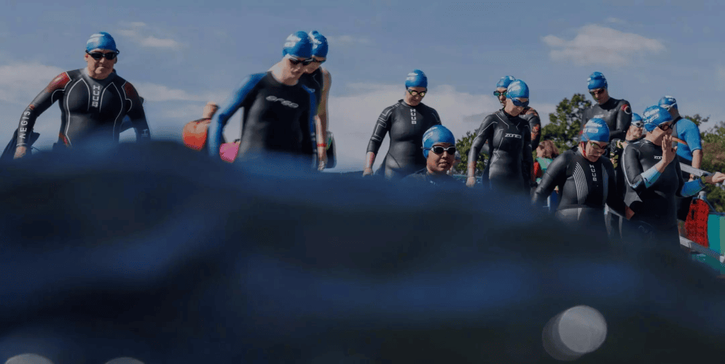 Photo of a group of people wearing swimming hats waiting to dive into the Serpentine Lake at Swim Serpentine.