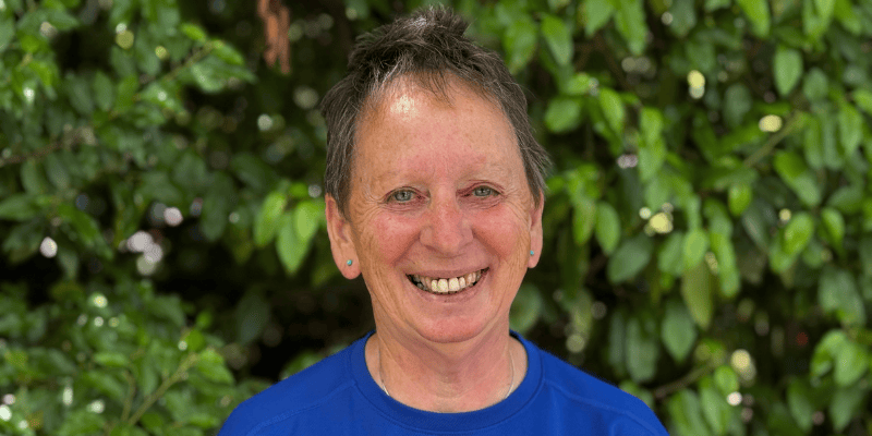 Photo of Rose smiling at the camera in front of some green foliage.