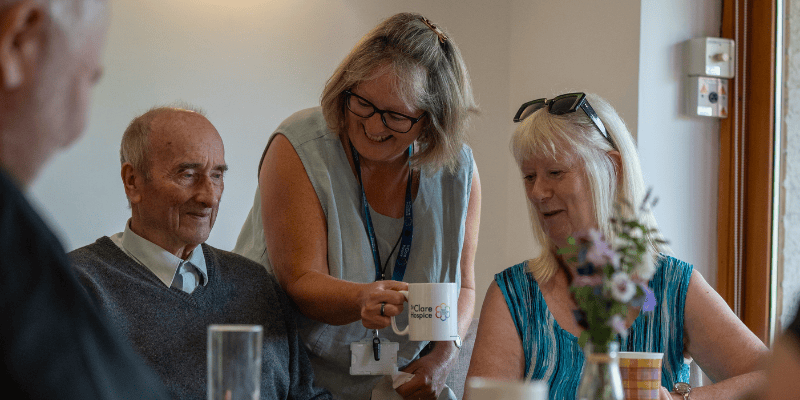 Photo of volunteer Café Clare facilitator Gail. She is serving cups of tea to people.