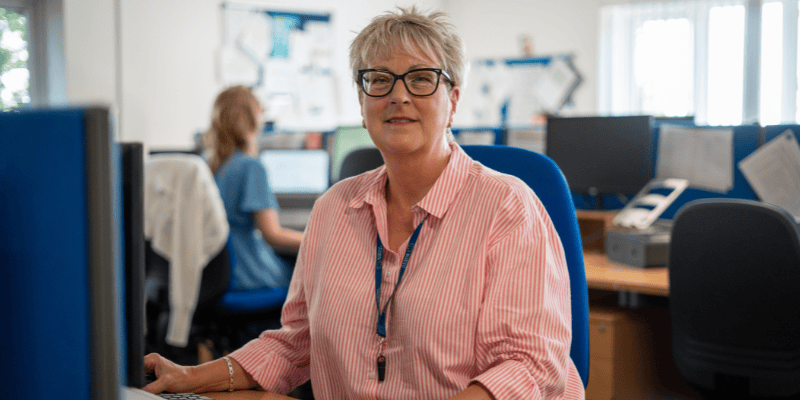 Photo of Hospice volunteer clinical admin Belinda at her desk. She smiles to camera.