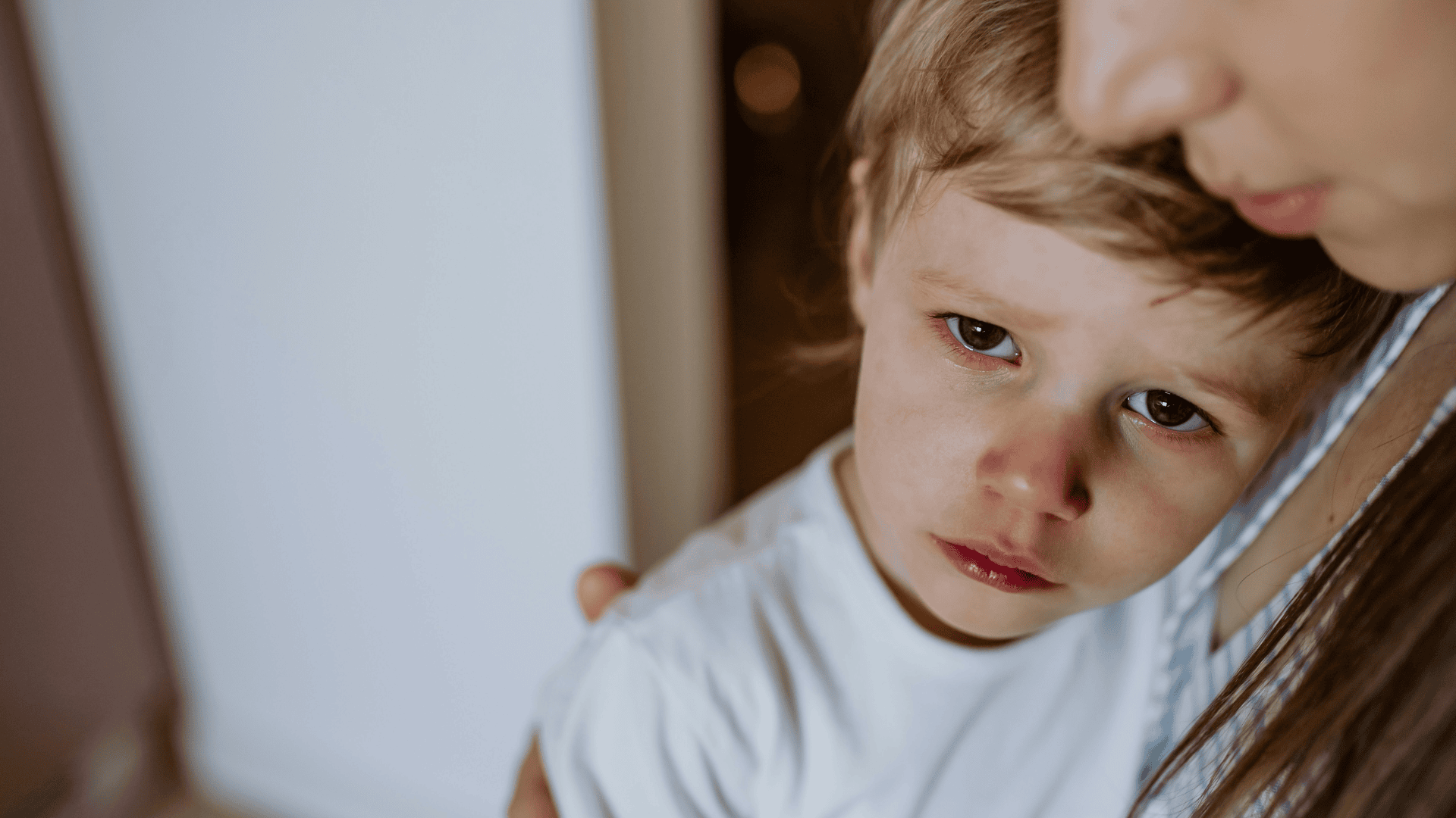Young boy is pictured with a sad look on his face while his parent/guardian comforts him.