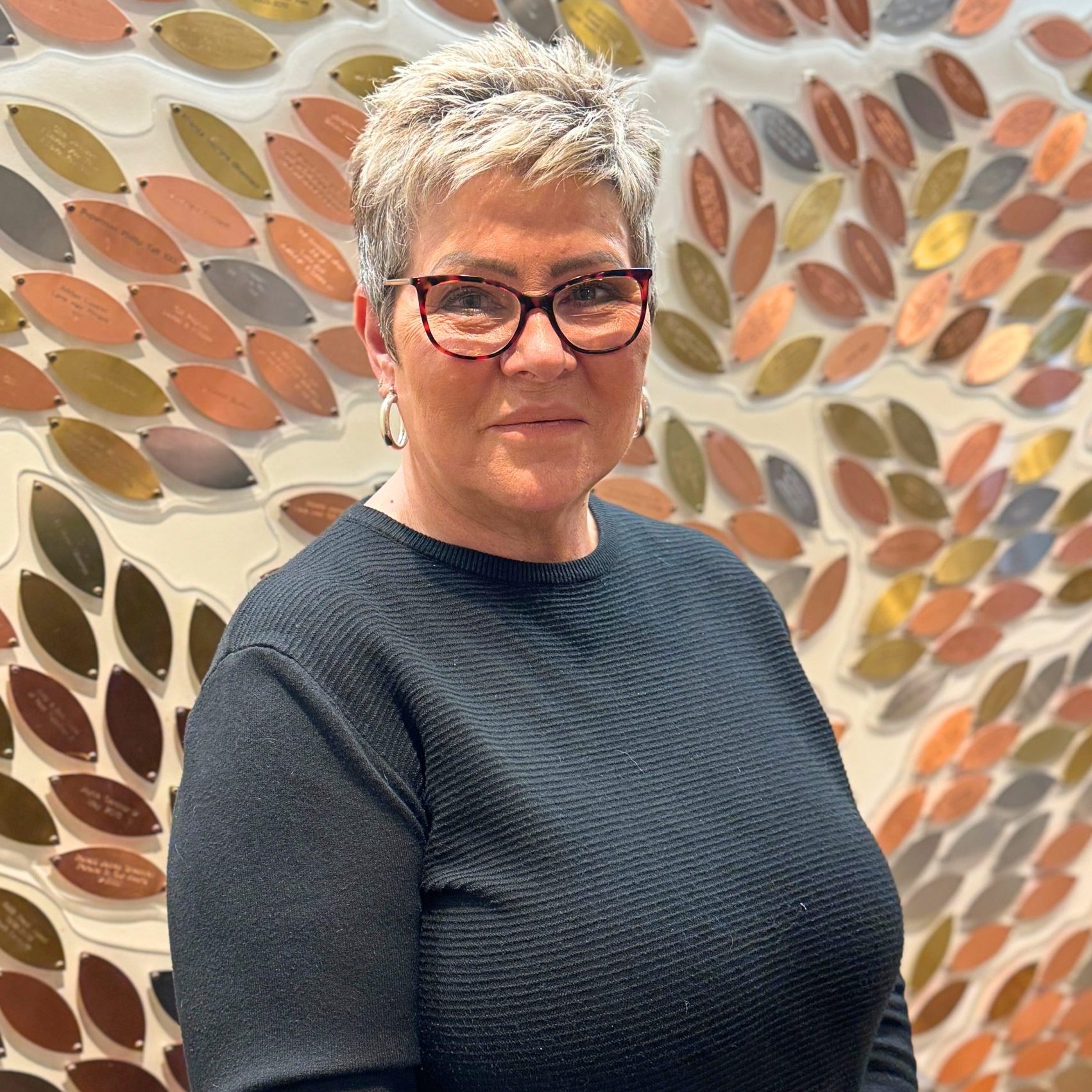Photo of June in front of the Memory Tree. She smiles.