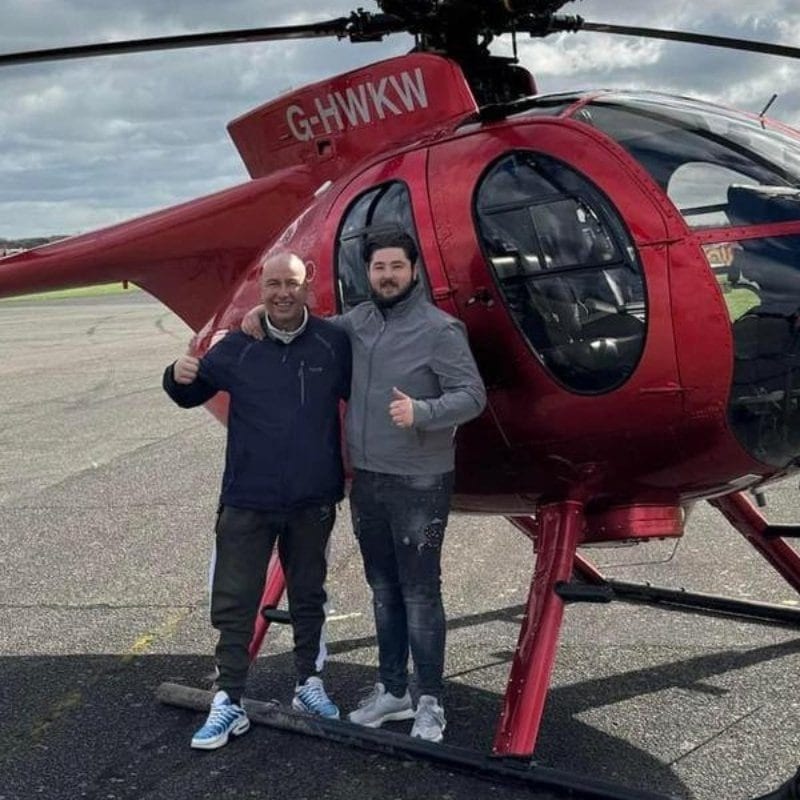 Photo of Bradley with his dad Bob in front of a helicopter. They both smile and hold their thumbs up to the camera.