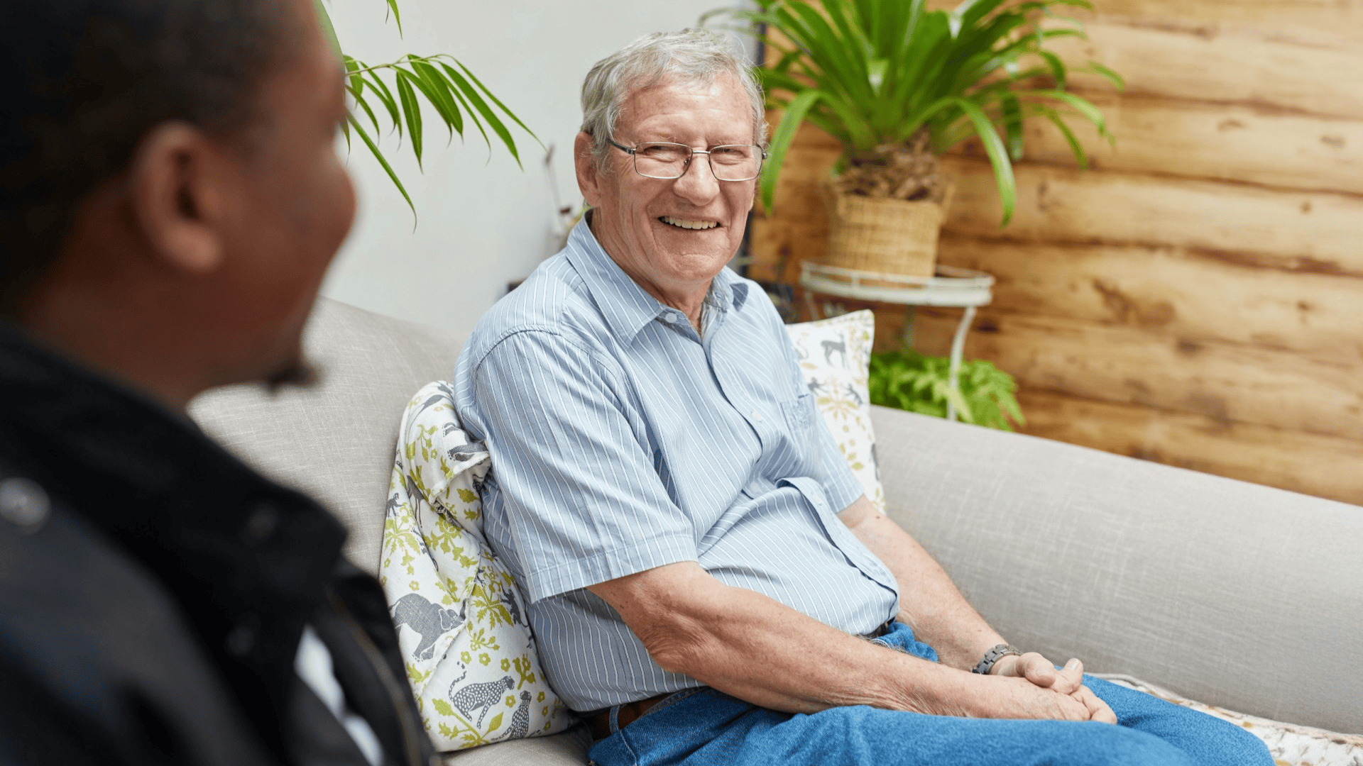 Photo of a male sat smiling on a sofa while chatting to a healthcare professional.